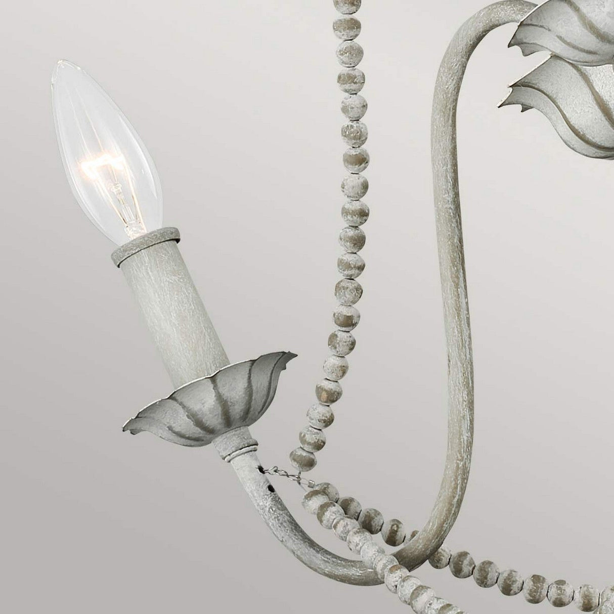 A close-up of a vintage-style chandelier arm featuring a candle-like bulb, embodying French Country elegance. The Maryville 3 Light Chandelier - Washed Grey boasts bead accents and a distressed wood appearance, set against a neutral backdrop.