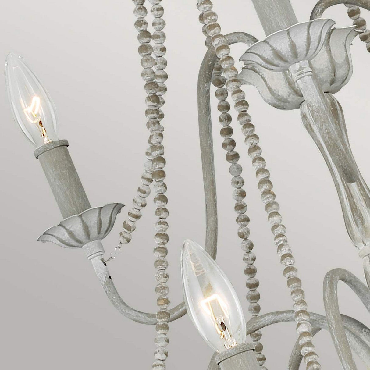 A close-up of the Maryville 9 Light Chandelier - Washed Grey highlights French Country sophistication with candle-shaped bulbs and decorative beading. The chandelier exudes rustic charm through its distressed, soft gray finish, blending elegance with a timeless, aged allure.