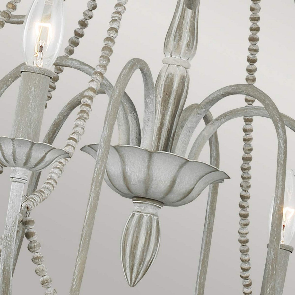 The Maryville 9 Light Chandelier - Washed Grey exudes rustic charm with its intricate metal detailing and gracefully curved arms. This chandelier is adorned with beaded strands and features multiple candle-like light bulbs, all finished in a weathered, antique style that embodies French Country sophistication.