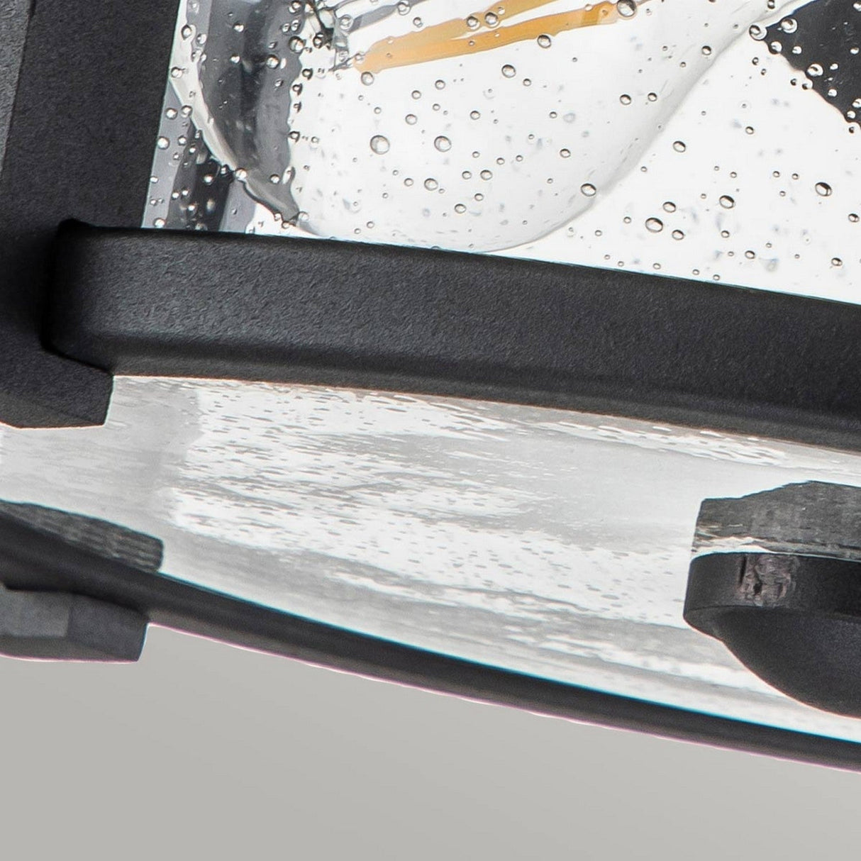 A close-up of the textured, curved Merrill 2 Light Outdoor Flush - Black featuring clear seeded glass and sophisticated black metal accents.