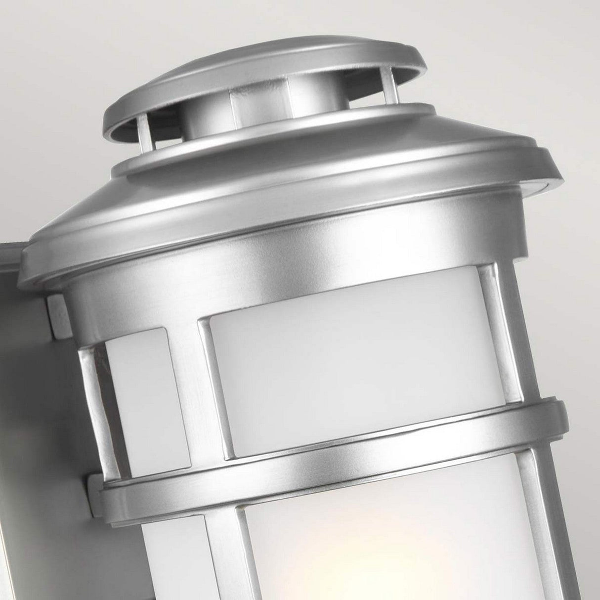 Close-up of the Newport 1 Light Outdoor Medium Wall Lantern in brushed steel, showcasing its coastal elegance. The sleek cylindrical design features a frosted glass panel and a slightly rounded top, mounted on a flat base, adding a touch of modern style to any exterior.