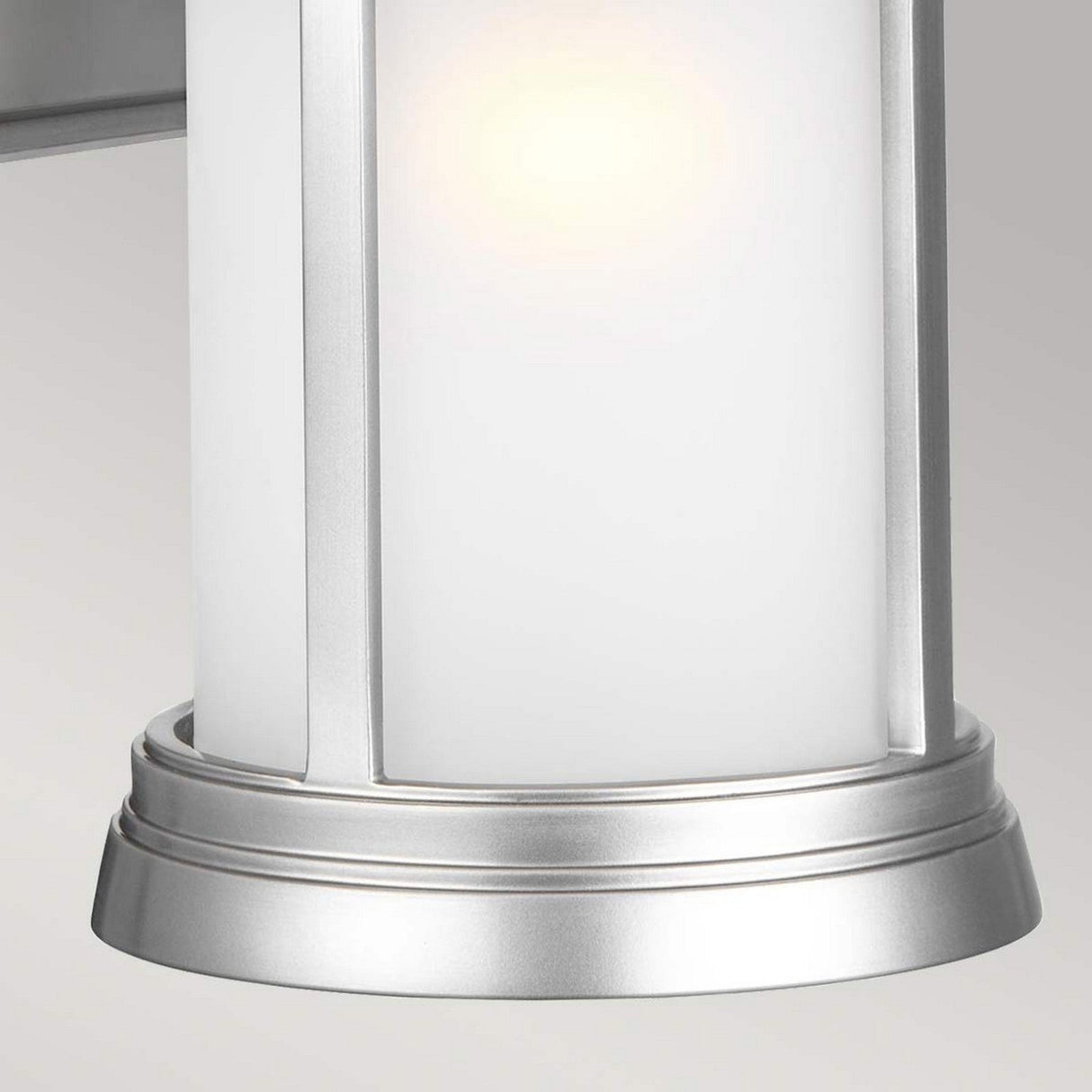 Close-up of the Newport 1 Light Outdoor Medium Wall Lantern in silver and white with a soft glow, featuring a brushed steel finish. The metallic base and trim enhance its modern appeal while maintaining coastal elegance. The background is a neutral gray.