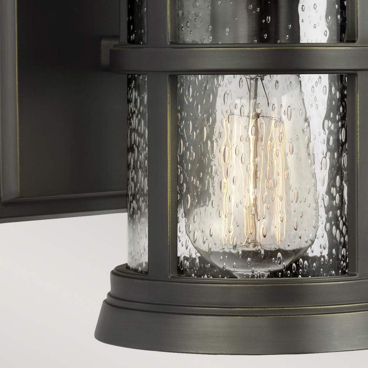 Capture the details of the Newport 1 Light Outdoor Small Wall Lantern, showcasing its antique bronze frame enveloping a cylindrical glass cover adorned with a bubble texture. The exposed filament bulb within shines warmly, crafting an inviting and cozy atmosphere ideal for coastal-style homes.