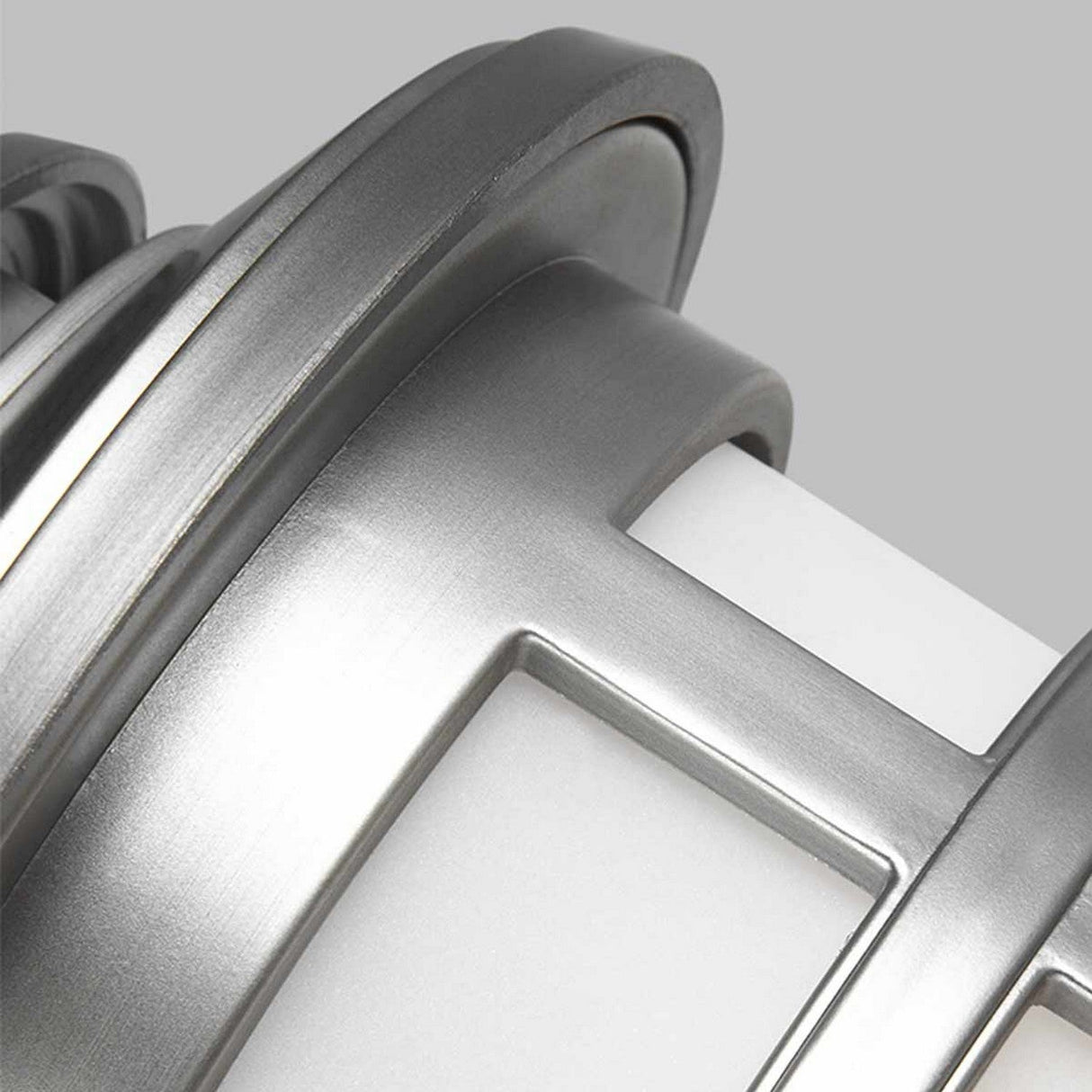 A close-up of the Newport 1 Light Outdoor Small Wall Lantern captures its coastal elegance through a modern metallic design. The cylindrical shape, crafted from brushed steel, showcases sleek silver-gray lines against a smooth white surface, embodying a minimalist and contemporary aesthetic.