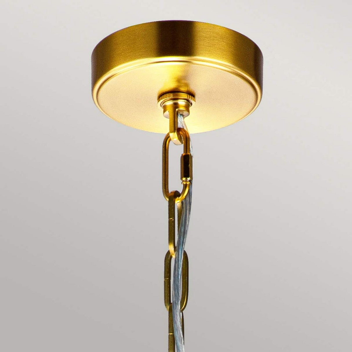 A close-up of the Nico 1 Light Large Pendant in burnished brass showcases its ceiling fixture with a chain link intertwined with an electrical cord, perfectly complementing its industrial décor style against a smooth, neutral-colored ceiling.