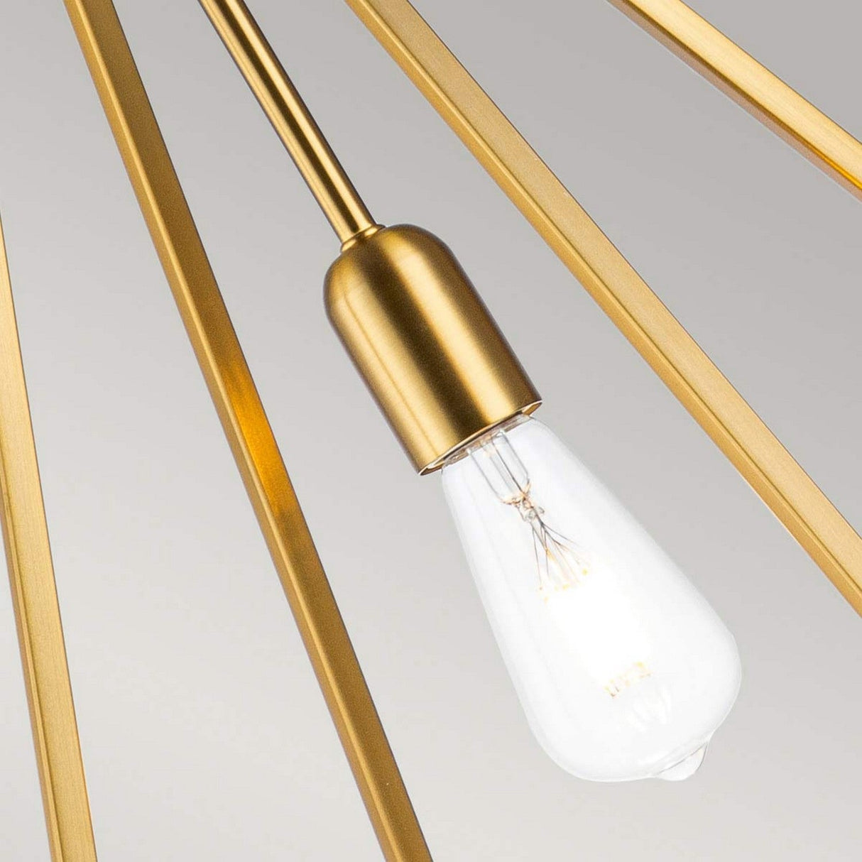 Close-up of the Nico 1 Light Large Pendant in Burnished Brass, showcasing a modern light fixture with a clear Edison-style bulb encased by gold rods. The soft grey background accentuates the minimalist elegance and industrial décor-inspired geometric artistry of the design.