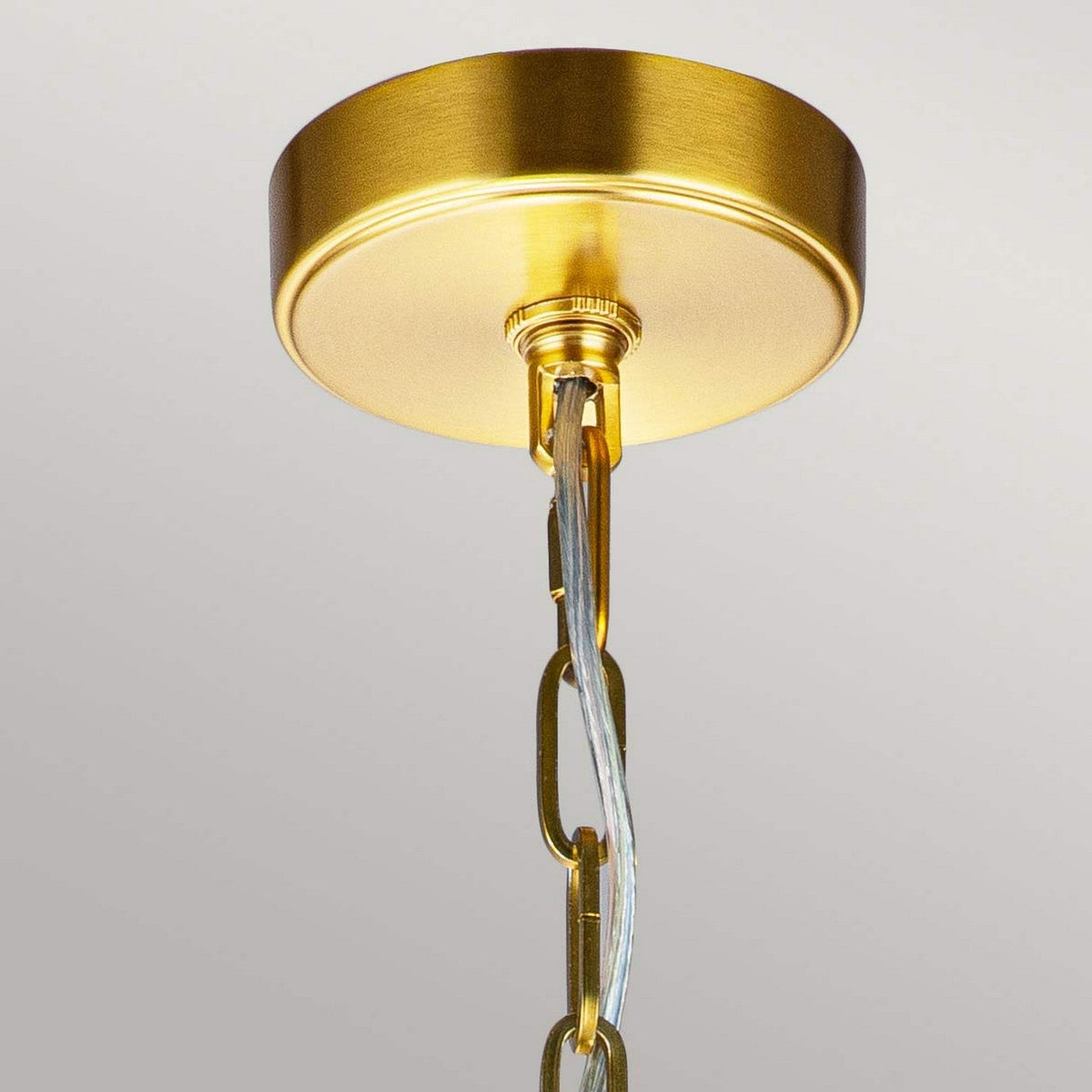 Close-up of the Nico 1 Light Medium Pendant in burnished brass, featuring a gold-colored ceiling mount with a chain supporting an electrical cord that exudes industrial charm. The pendant light's burnished brass finish enhances the metallic sheen to create a warm, elegant appearance.