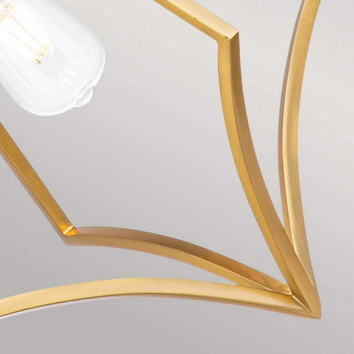 Close-up of the Nico 1 Light Medium Pendant in burnished brass, showcasing a modern geometric design with angular lines that converge at a central point. The pendant features an exposed bulb and is set against a neutral background.