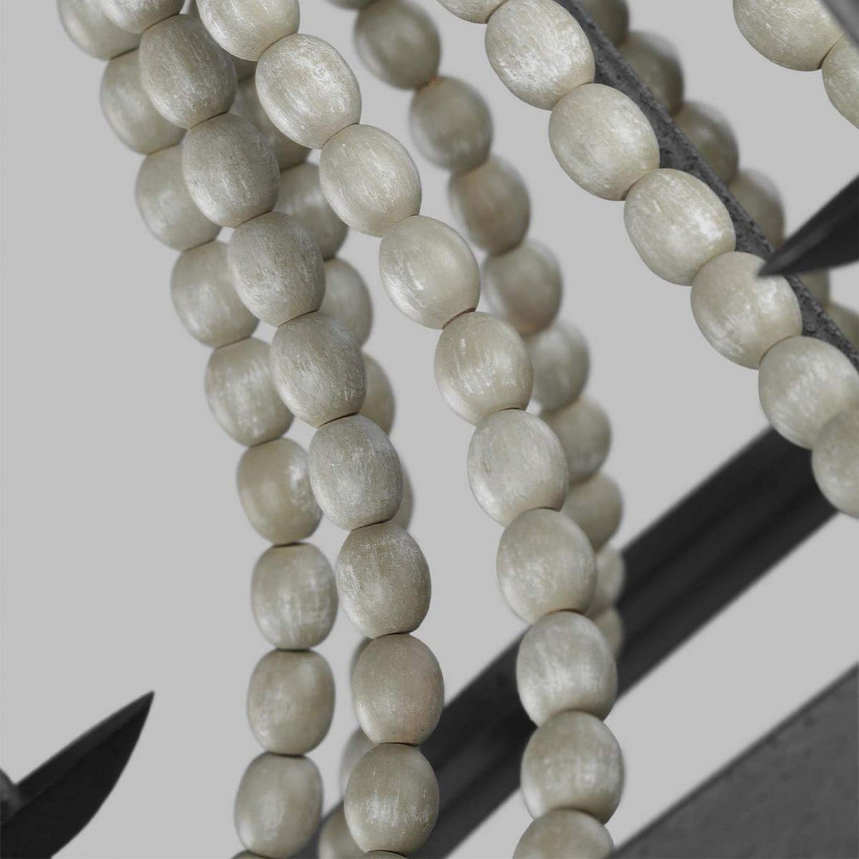 Close-up of several strands of smooth, cylindrical beige wooden beads hanging against a driftwood grey background. The evenly sized beads create a symmetrical and textured pattern reminiscent of the Dark Weathered Zinc Nori 3 Light Chandelier with Driftwood Grey accents.