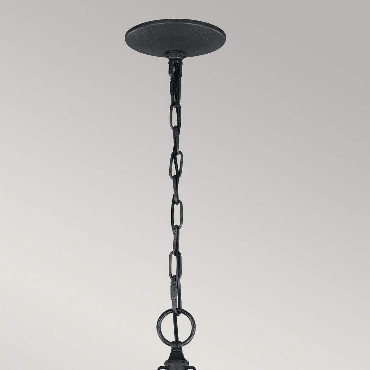 A black metal chain gracefully descends from a ceiling fixture in Dark Weathered Zinc with Driftwood Grey, casting delicate shadows against a plain gray background, reminiscent of the subtle sophistication of a Nori 3 Light Chandelier.