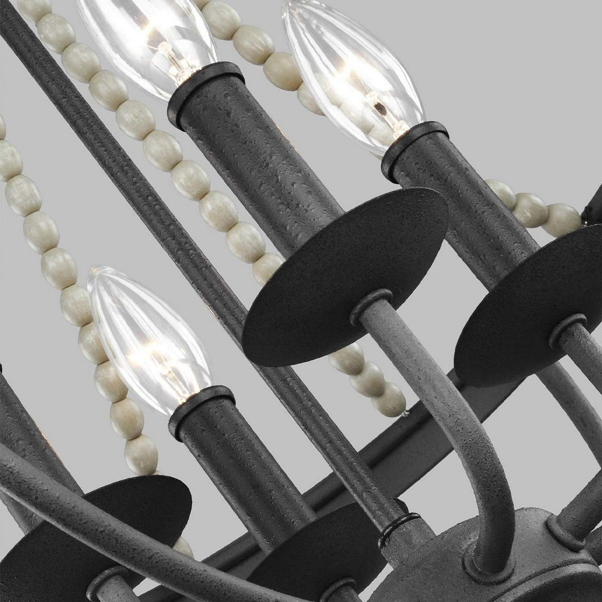 A detailed view of the Nori 4 Light Chandelier featuring candle-shaped bulbs and round bead-like accents. This modern and elegant piece showcases a Dark Weathered Zinc finish, complemented by a Driftwood Grey backdrop.