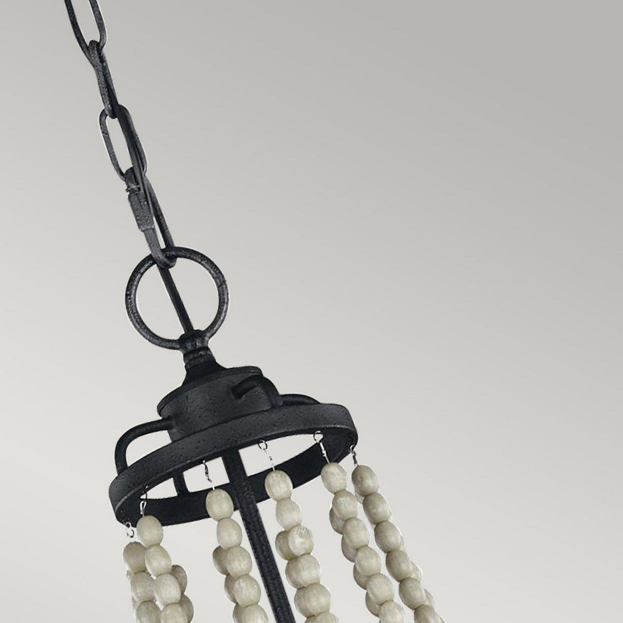 The Nori 4 Light Chandelier, with its dark weathered zinc finish and cascading white bead strands, hangs elegantly from the ceiling on a sturdy metal chain, perfectly complementing the Driftwood Grey backdrop.