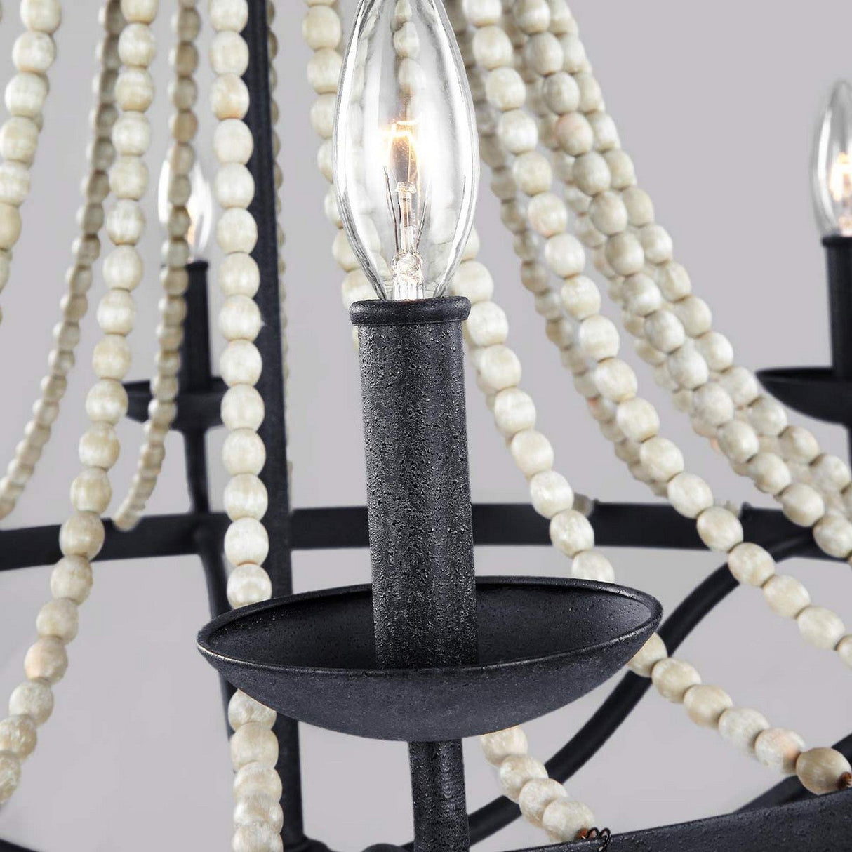 A close-up of the Nori 6 Light Chandelier - Dark Weathered Zinc With Driftwood Grey highlights its candle-like bulbs encircled by draped strands of round Driftwood Grey beads, creating a striking contrast against the Dark Weathered Zinc base while maintaining an elegant and soft aesthetic.