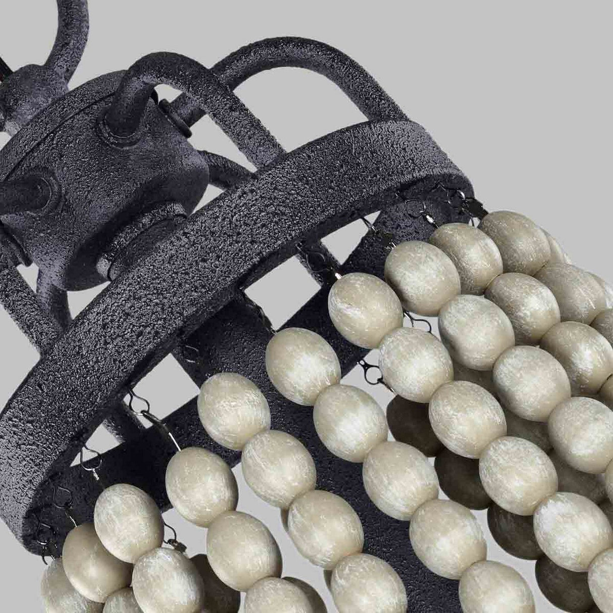 Close-up of the Nori 6 Light Chandelier - Dark Weathered Zinc With Driftwood Grey, highlighting its metal frame with a rustic finish. Pale, oval driftwood grey beads hang vertically in strands, forming a layered look against a neutral gray background that accentuates the dark weathered zinc accents.