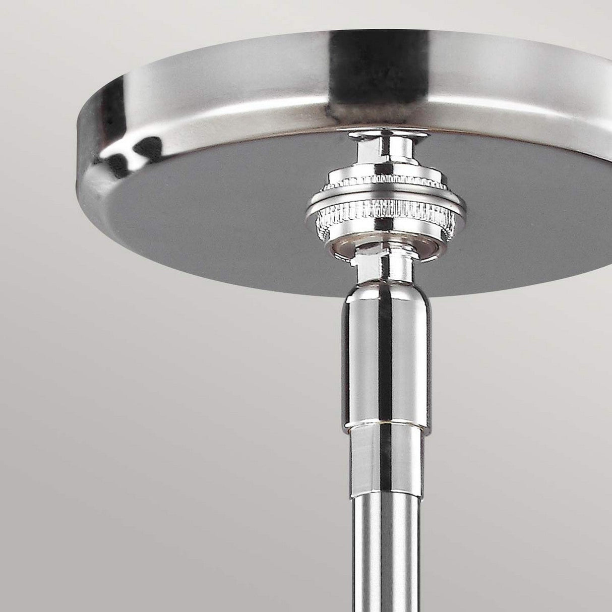Close-up of a chrome ceiling mount with a cylindrical metal rod extending downward, echoing the modern elegance of the Paulson 6 Light Pendant - Chrome. The rod showcases detailed grooves near the top, accentuated by glass tube shades against a neutral gray background.