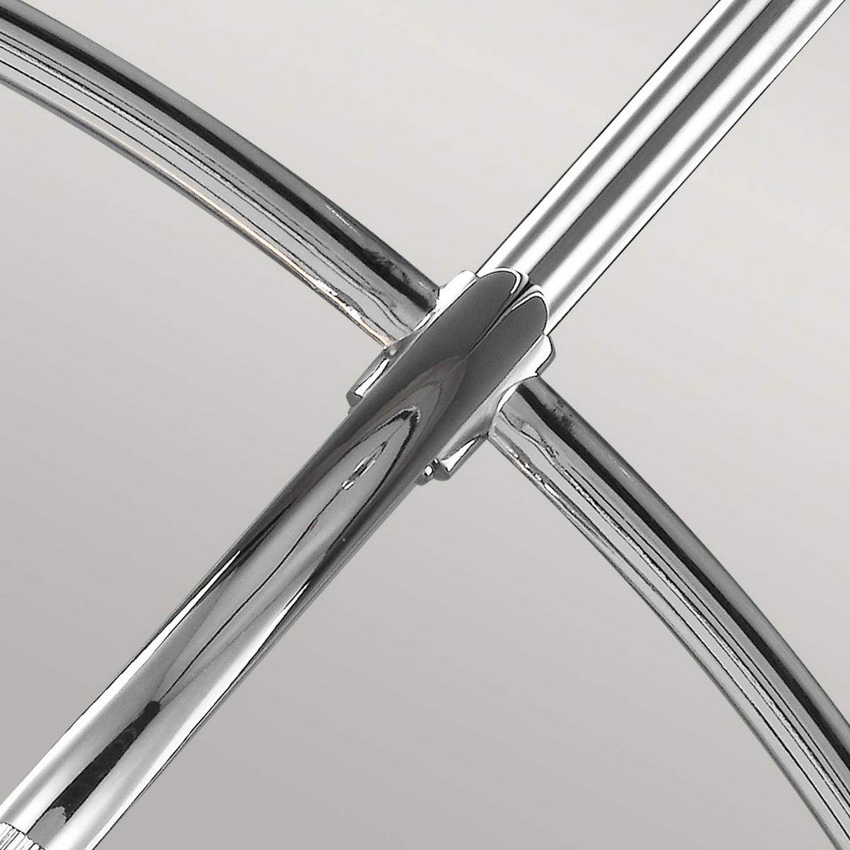A close-up view of a chrome metallic structure with intersecting cylindrical rods and a curved design showcases a sleek, modern aesthetic reminiscent of the Paulson 6 Light Pendant - Chrome. The light gray background highlights the reflective sheen of its chrome finish.