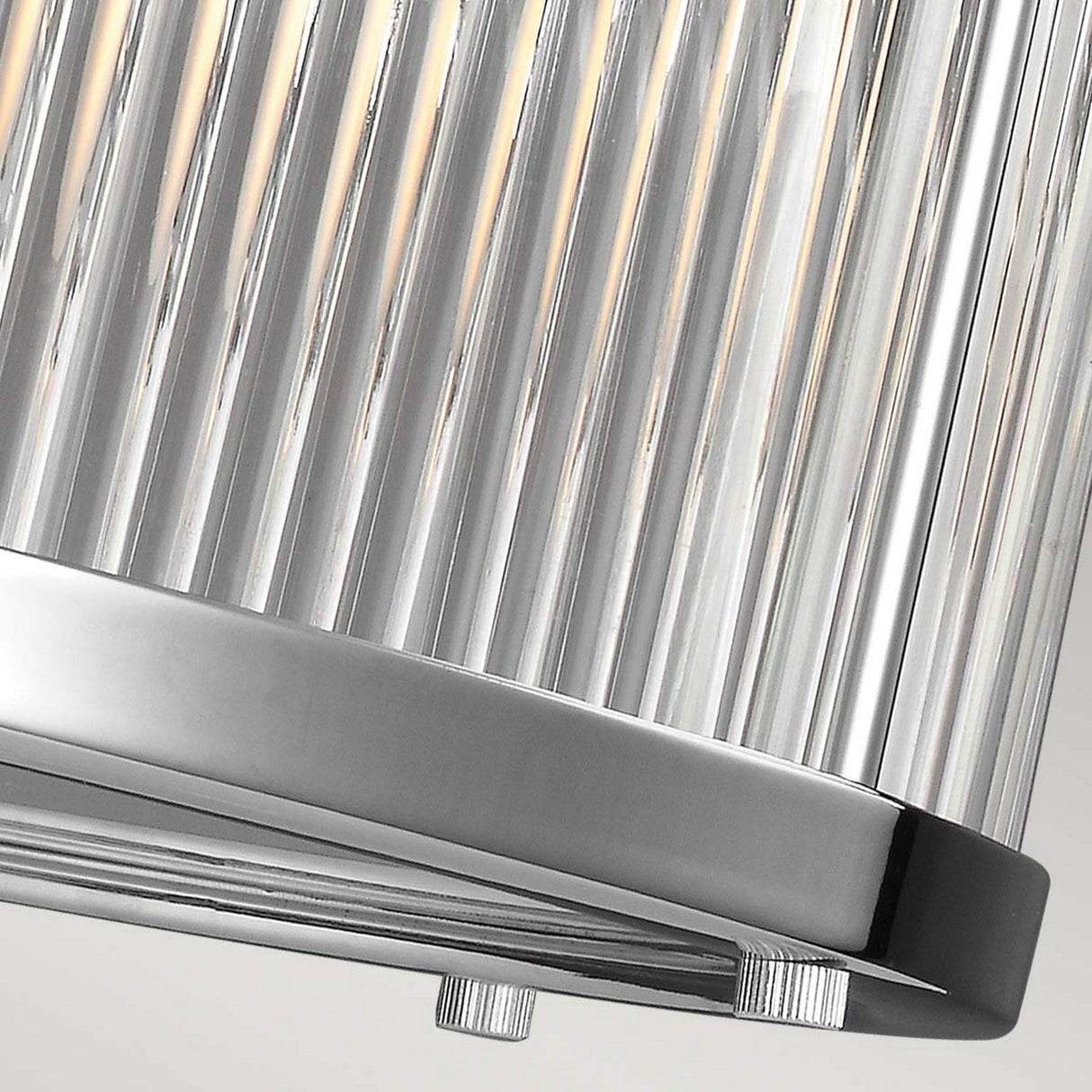 Close-up of the Paulson 6 Light Pendant - Chrome featuring vertical metallic slats with a chrome-like finish. Warm glowing light shines through the slats, complemented by elegant glass tube shades and a sleek, reflective bottom edge that enhances its sophisticated design.