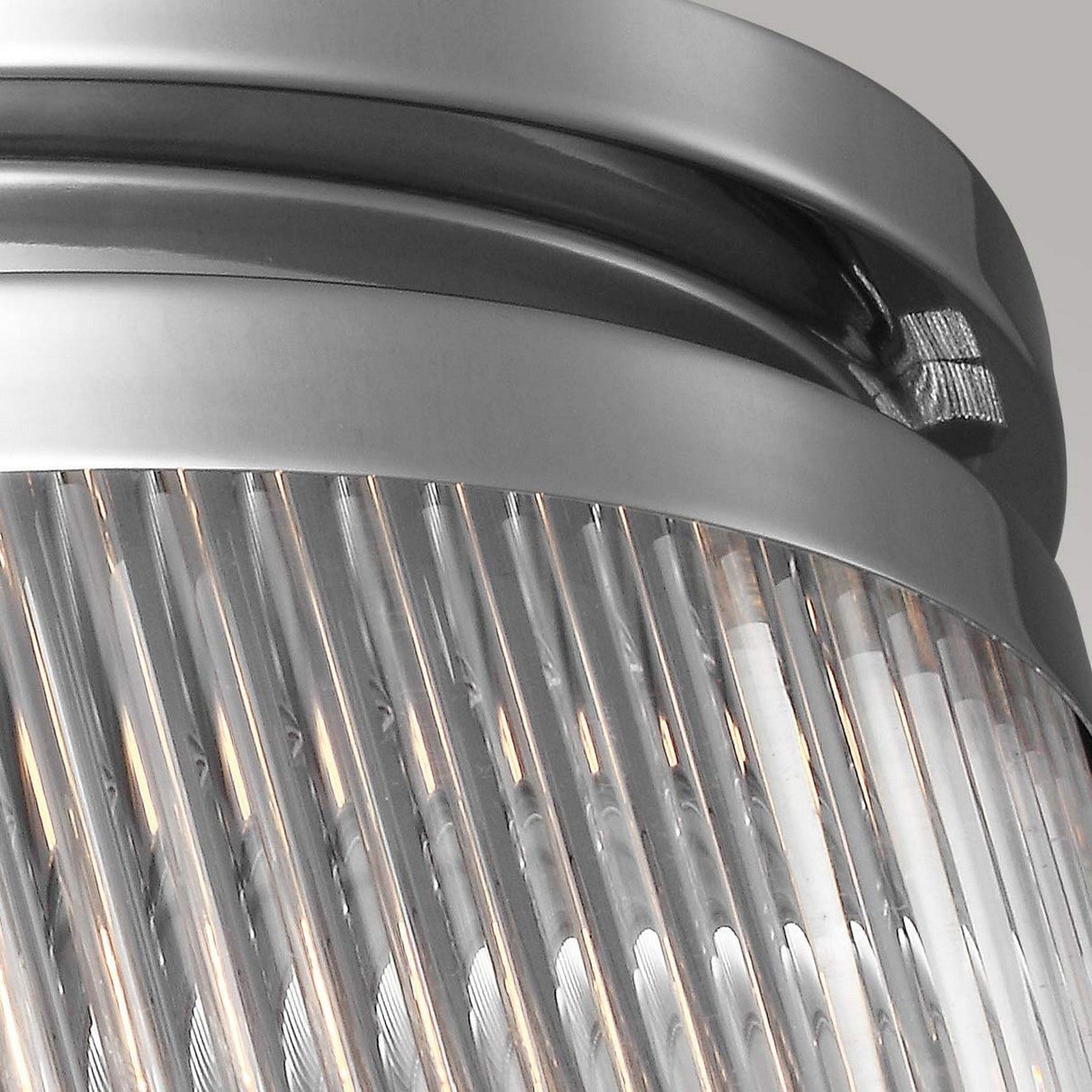 Close-up of a metallic ceiling light fixture characterized by clear glass rods and vertical, ridged panels in a sleek, modern design. The Paulson 3 Light Flush - Chrome features a polished finish that emits a soft glow.