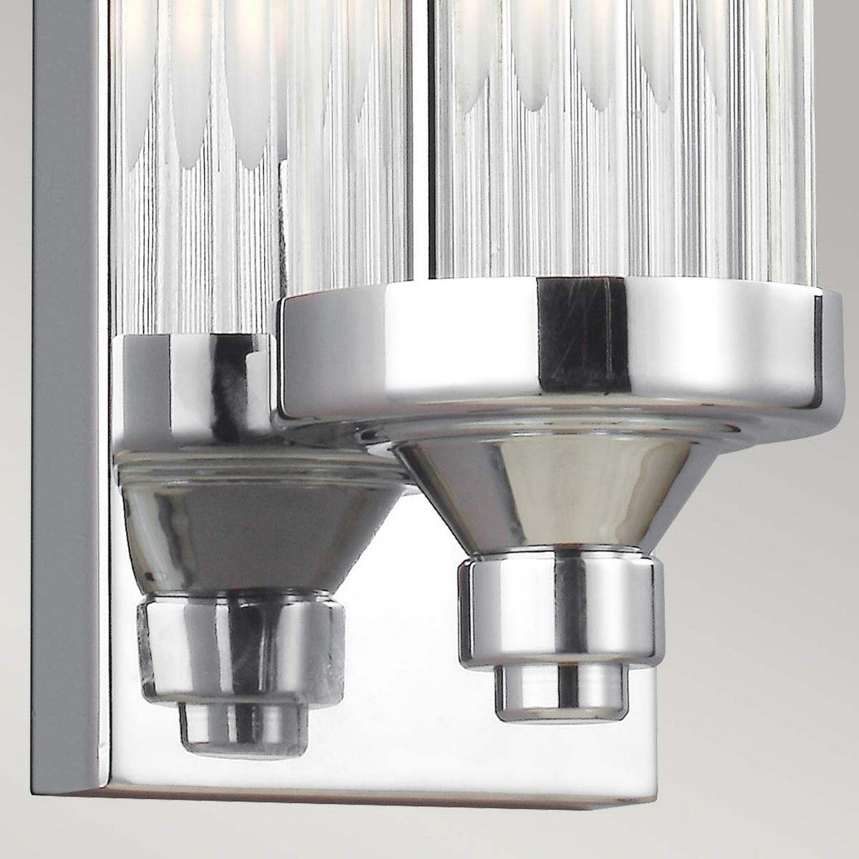 A close-up of the Paulson 4 Light Bar Light - Chrome displays its two metallic holders, each supporting clear, textured glass tube shades. The design is modern and sleek with a reflective chrome finish.