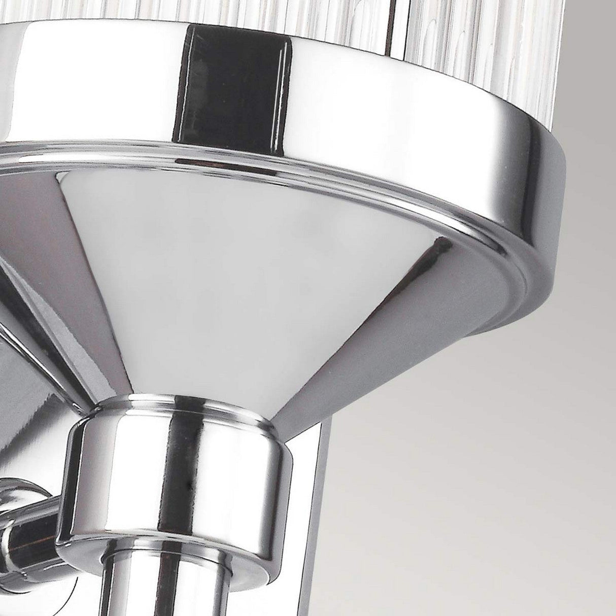 Close-up of the Paulson 1 Light Wall Light in chrome, showcasing a sleek conical design. The fixture features polished surfaces and a ribbed glass tube shade that elegantly reflects light. With an IP44 rating for bathroom use, it complements the neutral background to accentuate its glossy metal finish.