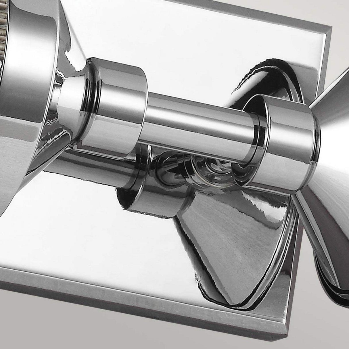 The Paulson 2 Light Bar Light in Chrome showcases sleek lines and reflective surfaces, enhancing its modern aesthetic. The shiny chrome finish and vintage design elements are highlighted as it is mounted on a rectangular base against a light-colored wall.