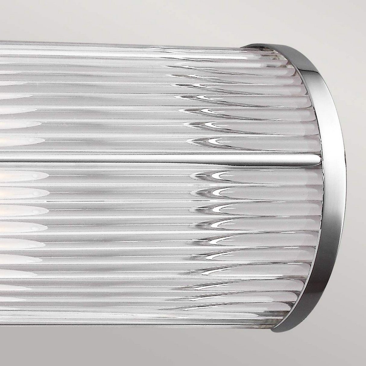 The Paulson 2 Light Bar Light - Chrome, with its cylindrical glass wall sconce and ribbed texture, is installed on a light-colored wall. This design showcases vertical lines and a sleek, modern aesthetic.