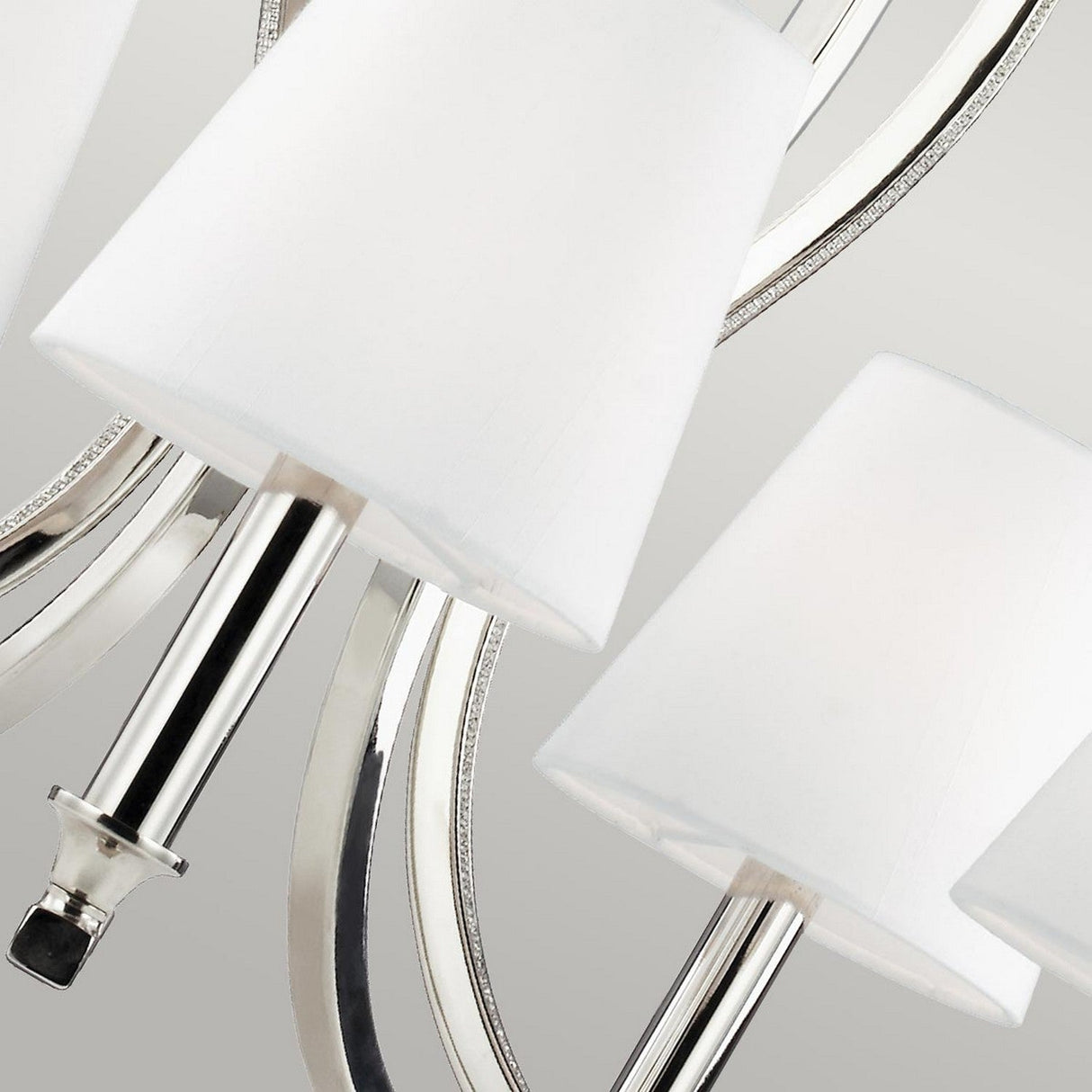 Close-up of the Pave 5 Light Chandelier - Polished Nickel, showcasing its sleek, overlapping silver arcs and trio of white lampshades. The polished nickel finish and crystal inlay contribute to its minimalist elegance, with smooth, reflective surfaces that enhance its contemporary aesthetic.