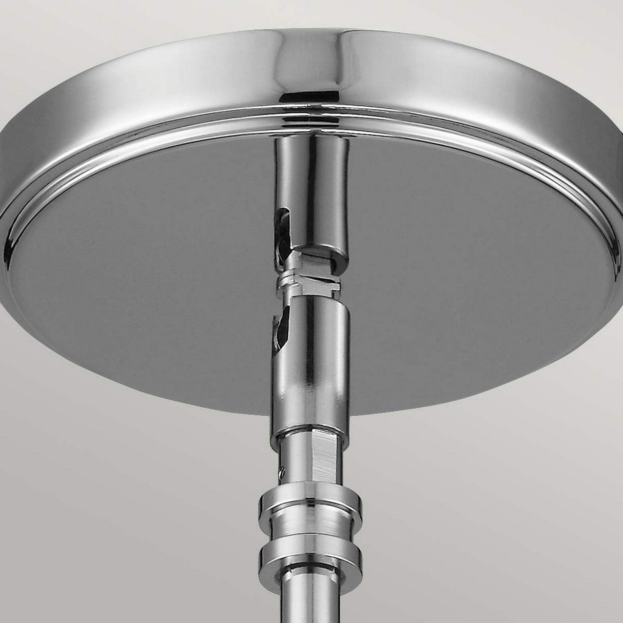 Close-up of the Payne 1 Light Mini Pendant – Polished Chrome, featuring a shiny chrome ceiling fixture with a circular base. The polished chrome finish offers a reflective and gleaming surface. This mini pendant is connected to a vertical rod, incorporating modern and sleek design elements against a light background.
