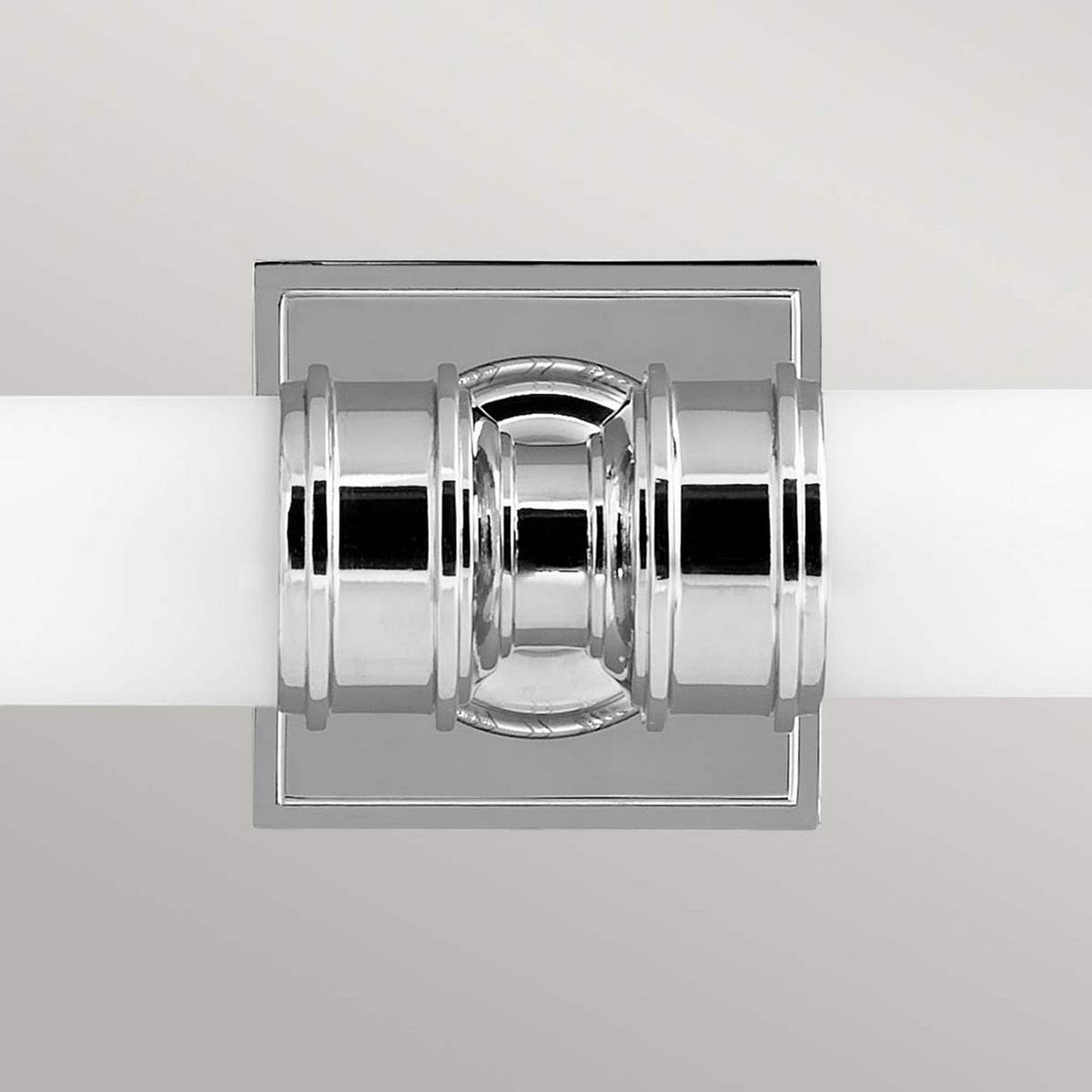 A Payne-2 2 Light Wall Light in polished chrome finish is mounted on a light gray wall, showcasing a design with cylindrical and geometric features that blend effortlessly with an English Tudor style, providing a modern and sleek look.