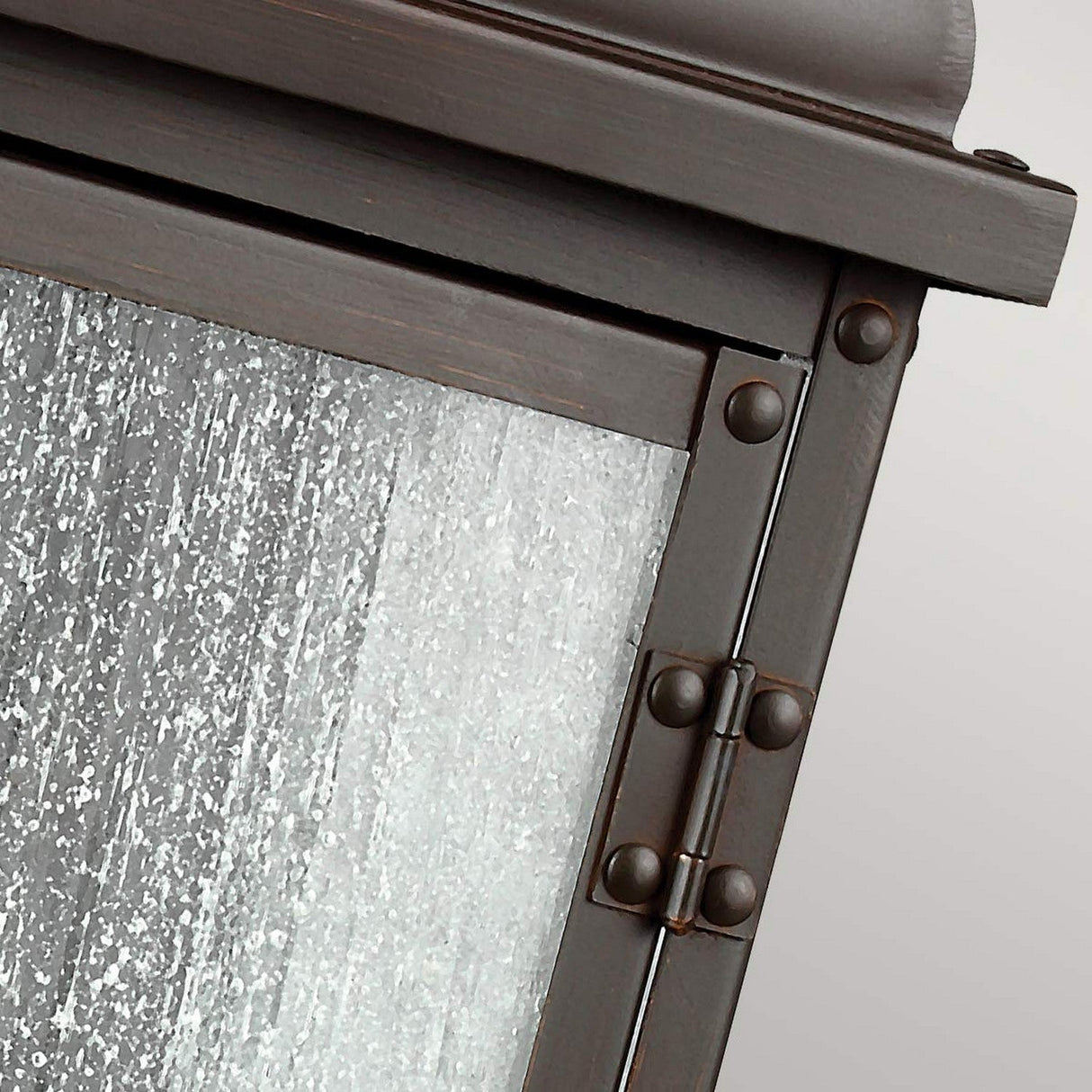 Close-up of the Pediment 2 Light Outdoor Medium Wall Lantern in Dark Copper, showcasing a rectangular metal frame with visible rivets and a right-side hinge. The glass panel has a weathered, textured appearance reminiscent of seeded glass.