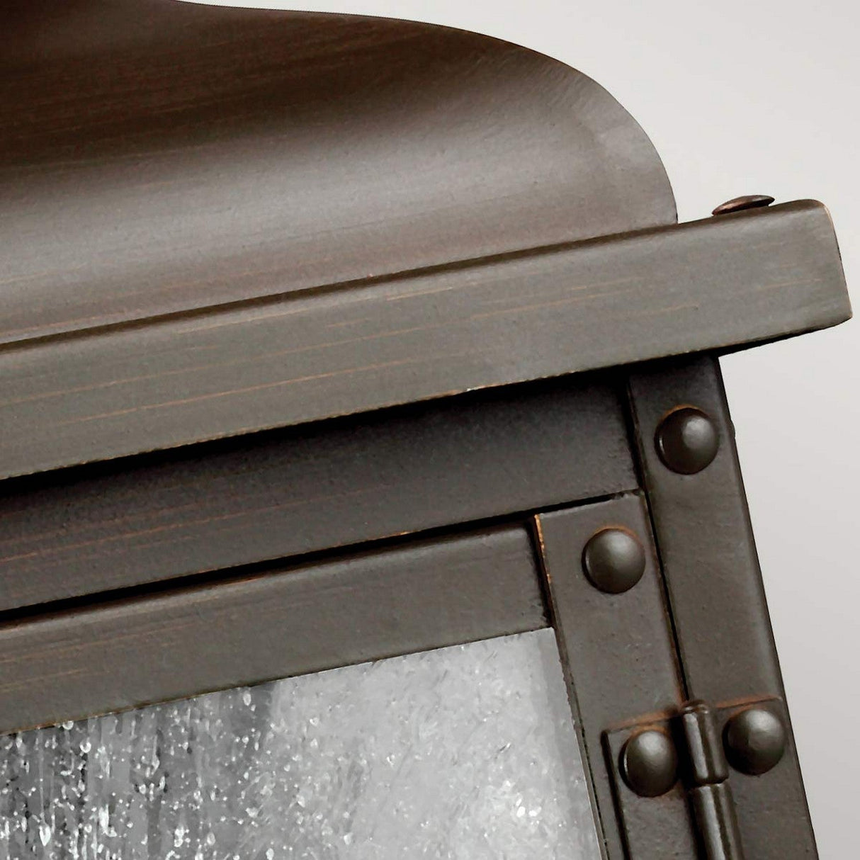 Close-up of the Pediment 2 Light Outdoor Small Wall Lantern in dark copper, featuring a flat top and rivet details on its frame. The textured seeded glass panel gives it a frosted appearance, set against a plain, light-colored background.