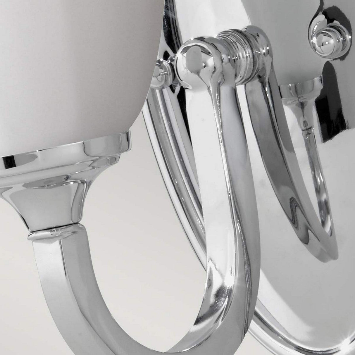 A close-up view of the Perry 1 Light Wall Light in polished chrome showcases its elegant curved arm and cylindrical opal glass shade. Mounted on a circular backplate, this wall light exudes a sleek and sophisticated look as it reflects the light beautifully.