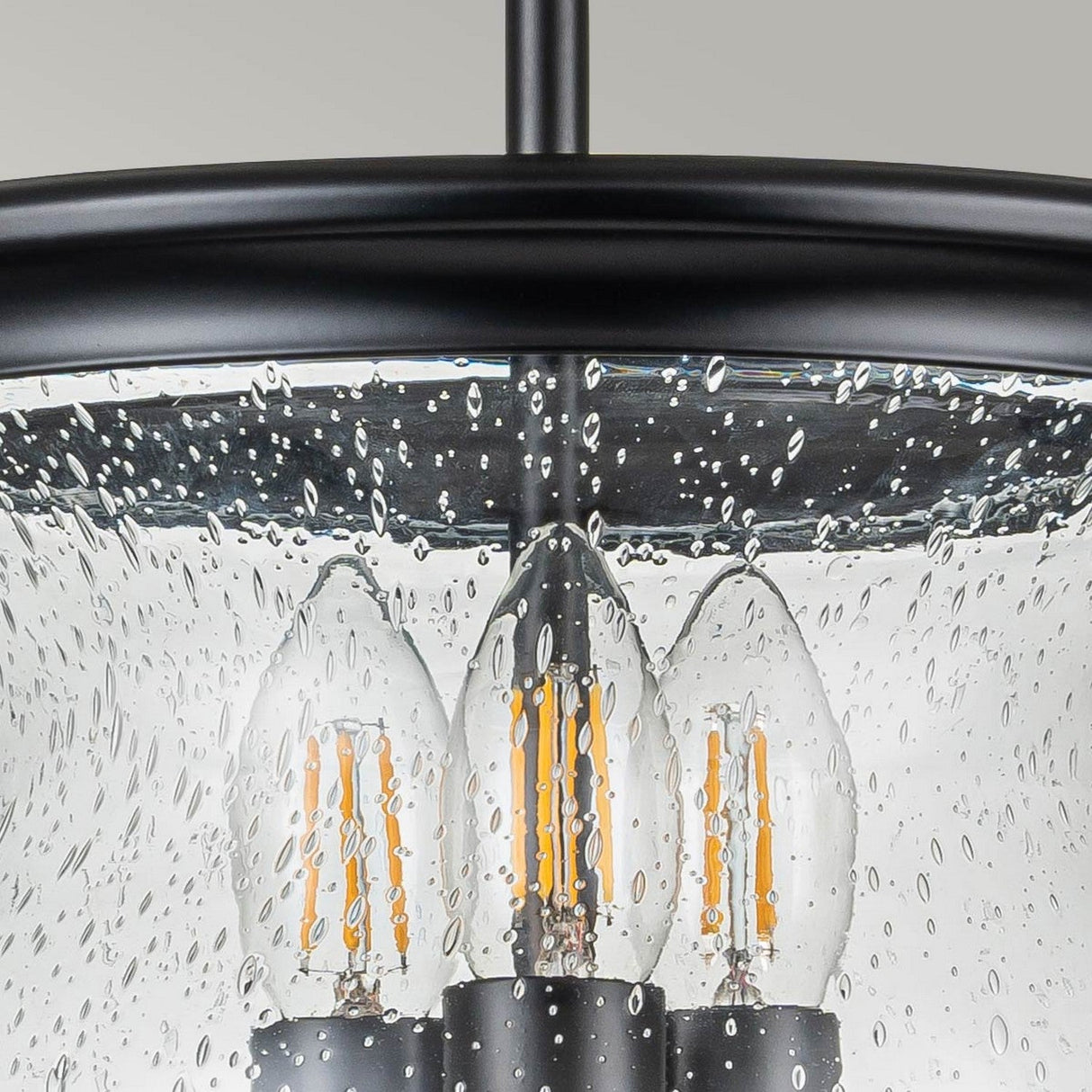 Close-up of the Pickering Lane 3 Light Semi Flush in Black, showcasing a round metal frame with candle-style bulbs. The seeded glass shade, adorned with raindrop patterns, beautifully complements the neutral background.