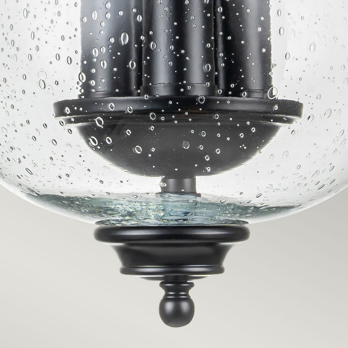 Close-up of the Pickering Lane 3 Light Semi Flush in black, showcasing a glass pendant light fixture. The clear seeded glass shade has a bubbled texture that adds a decorative touch to the design. Candle-style bulbs elevate its elegance against a softly blurred white background.