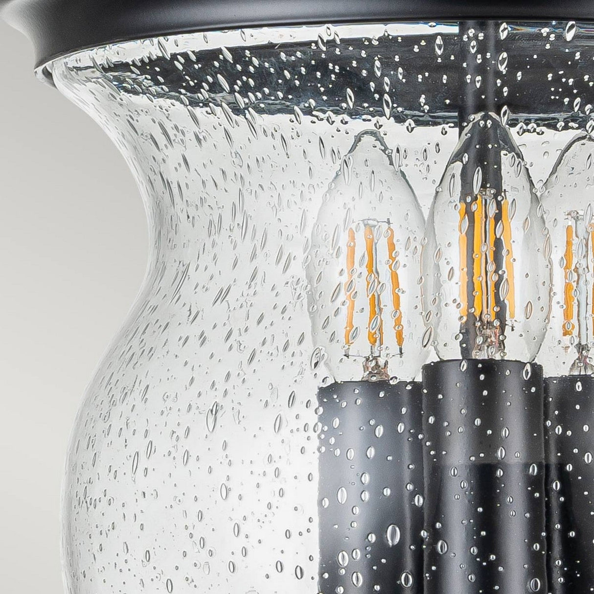 Close-up of the Pickering Lane 3 Light Semi Flush - Black, showcasing its seeded glass shade and three candle-style LED bulbs within. The glass features an elegant, curved design that contributes to a sophisticated and modern look against a neutral background.