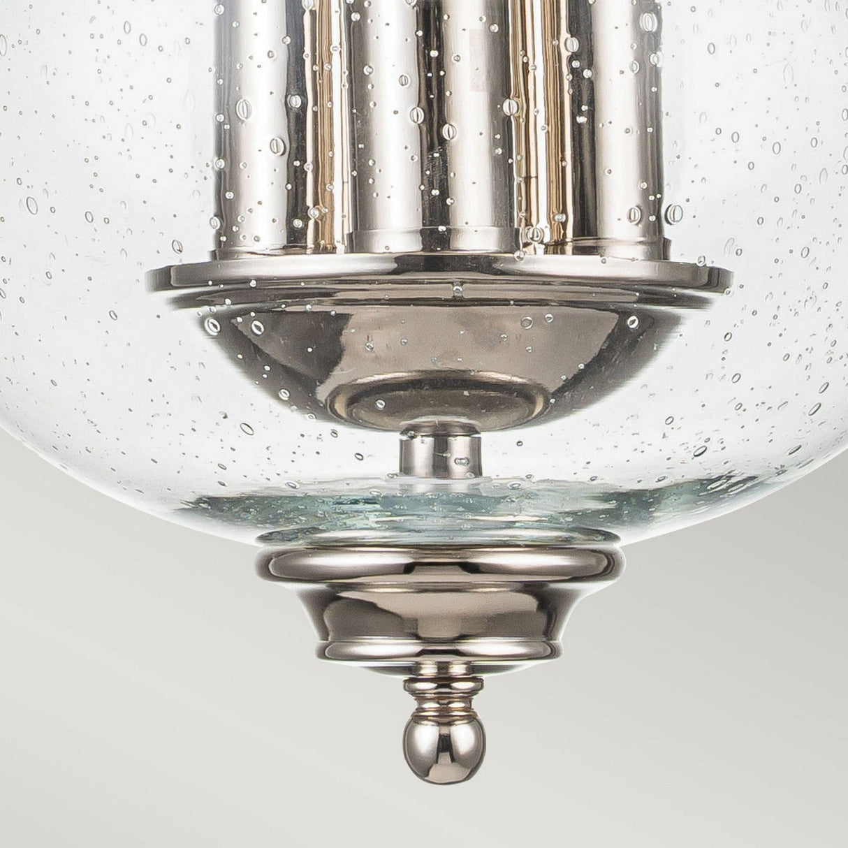A close-up view of the Pickering Lane 3 Light Semi Flush in Polished Nickel highlights its modern glass pendant light design, ideal for farmhouse lighting. The clear glass, adorned with small bubbles, complements its shiny, silvery metal finish.