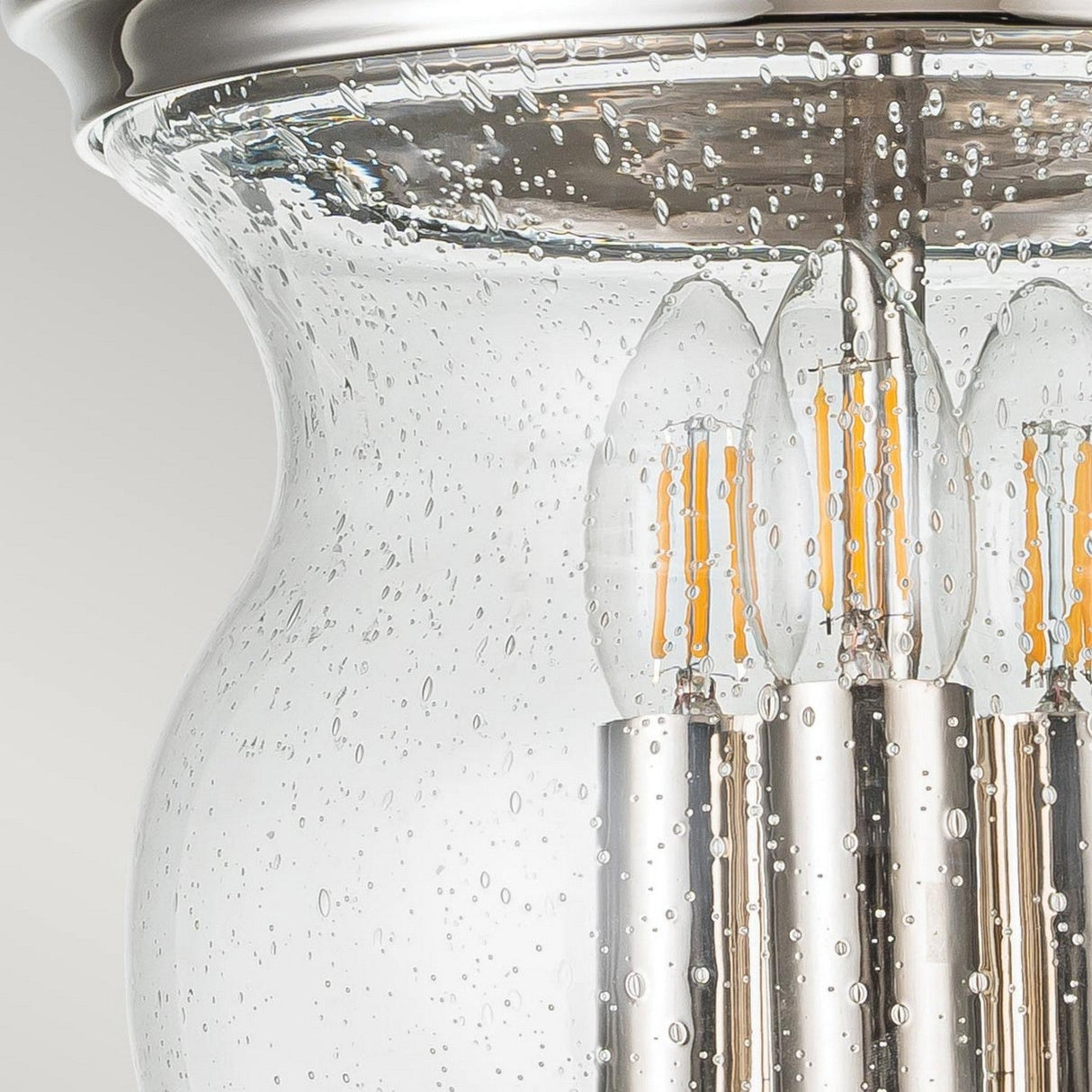 A close-up of the Pickering Lane 3 Light Semi Flush in Polished Nickel, featuring three LED bulbs surrounded by clear, textured glass. The glass, highlighted with small bubbles, enhances the modern silver metal design's stylish detail and polished nickel finish.