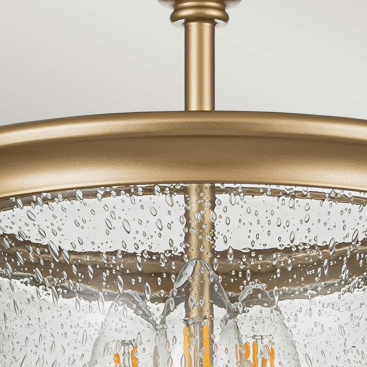 Close-up of the Pickering Lane 3 Light Semi Flush - Brass ceiling fixture, featuring a vintage appeal through its textured bubble-patterned glass shade. Inside the seeded glass, the visible filament bulbs emit a warm glow.