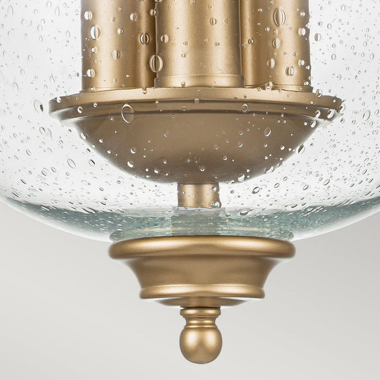Close-up of the Pickering Lane 3 Light Semi Flush fixture, showcasing a modern design with a brushed gold finish. The clear, seeded glass shade features intricate bubble-like patterns, complemented by smooth, curved lines and a polished base for an elegant touch with hints of vintage charm.