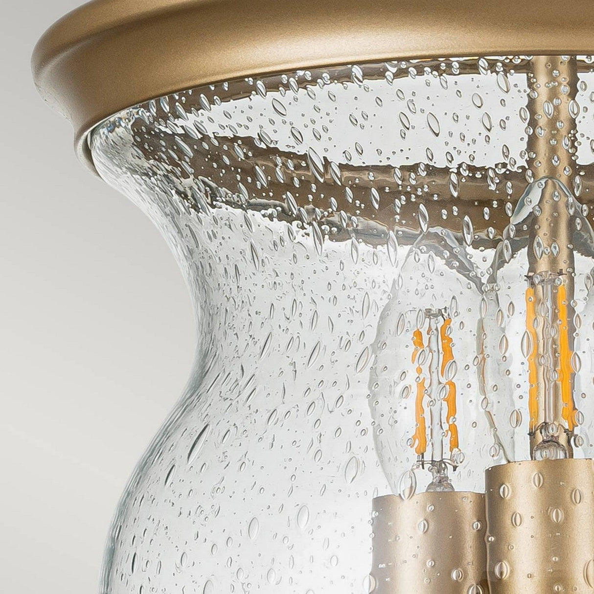 Close-up of the Pickering Lane 3 Light Semi Flush fixture featuring a brass finish that exudes vintage charm. The seeded glass shade is adorned with small bubbles, revealing LED filament bulbs inside that cast a warm glow.