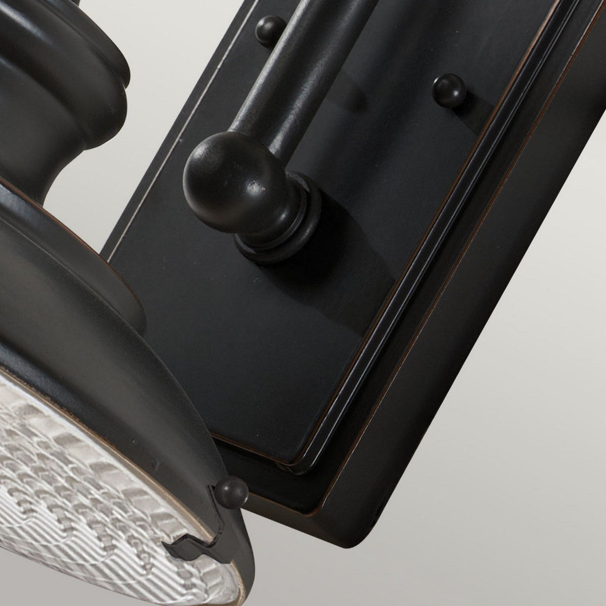 Close-up of the Redding Station 1 Light Outdoor Medium Wall Lantern in a wall-mounted black design, featuring a round, textured glass shade. This classic light fixture showcases a dark bronze finish with decorative elements on the base. Ideal for outdoor use, its weather-resistant construction complements the plain, light grey background.