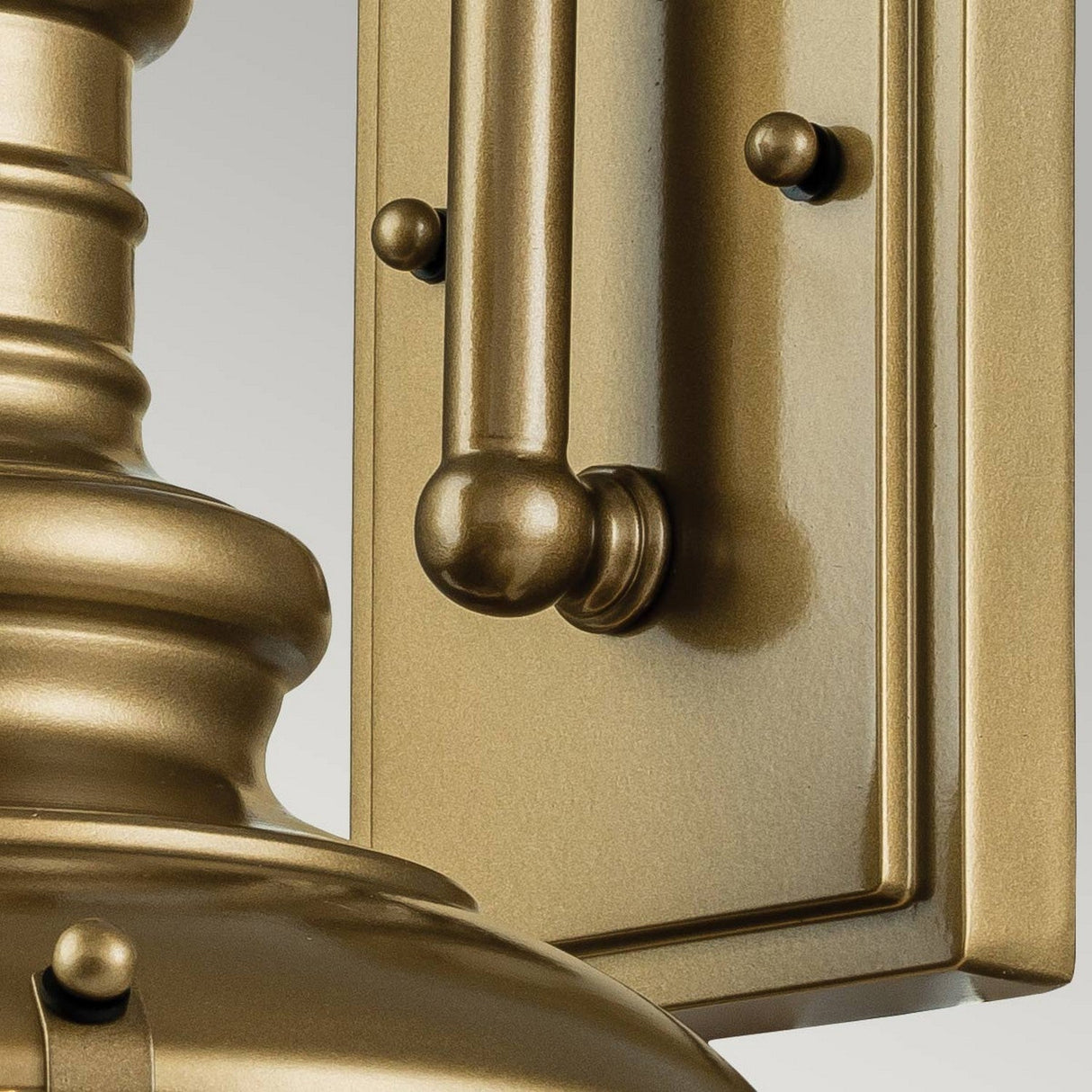 Close-up of the Redding Station 1 Light Outdoor Small Wall Lantern, highlighting a metallic frame adorned with decorative knobs and elegant, curved lines. The fixture boasts a warm bronze finish, and the photo captures the intricate, polished details of its design, complemented by a delicate prismatic glass shade.