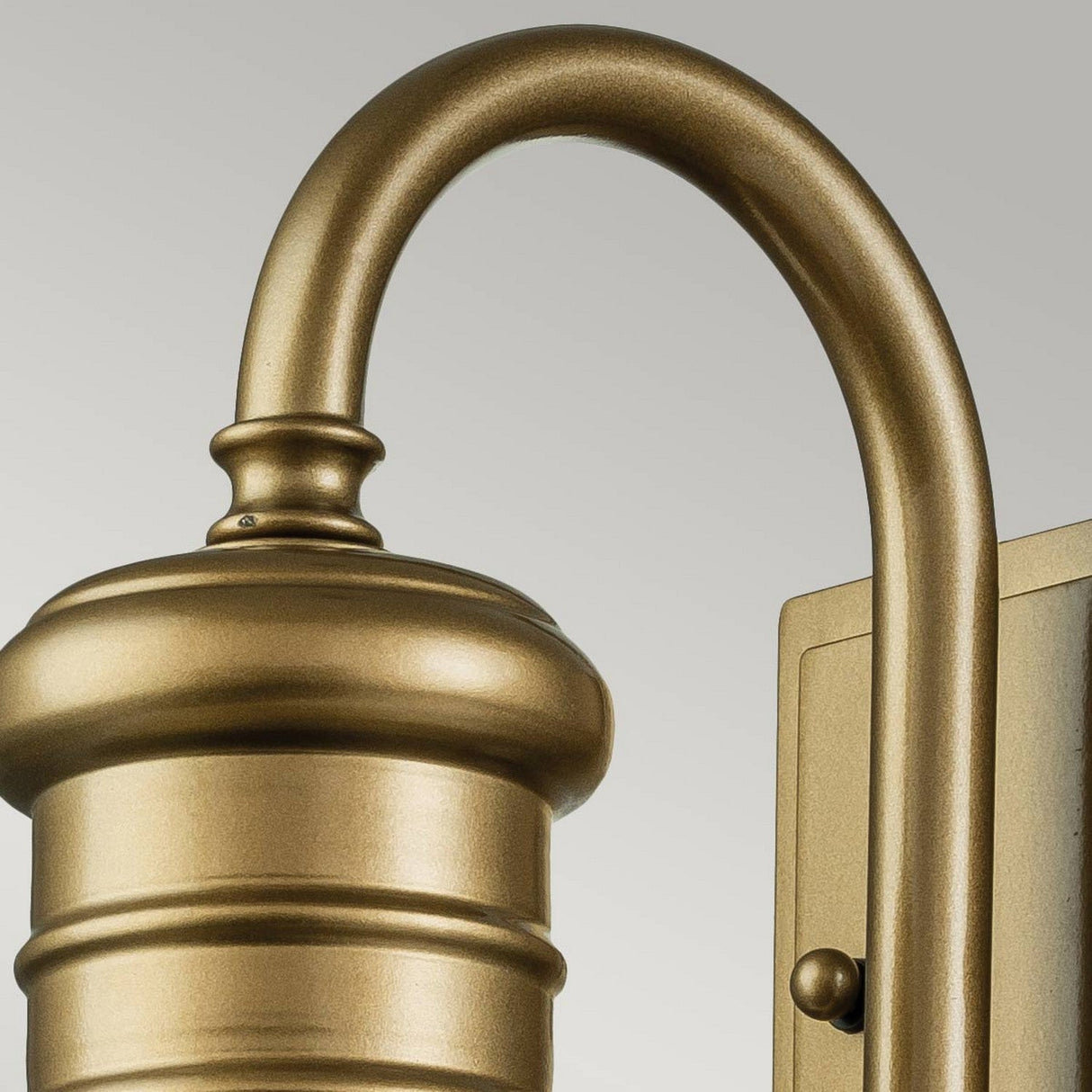 Close-up of the Redding Station 1 Light Outdoor Small Wall Lantern in a bronze finish, featuring a curved arm and a prismatic glass shade, set against a light gray background. This fixture exudes a classic and elegant design.