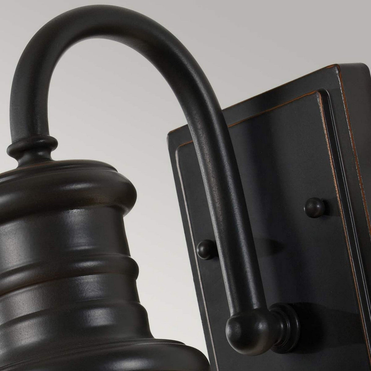 Here is a close-up description of the Redding Station 1 Light Outdoor Small Wall Lantern in dark bronze: It features a prismatic glass shade and is equipped with a curved arm and rectangular backplate, making it perfect for wall mounting. The lantern boasts a traditional round top with decorative grooves that enhance its elegant design.