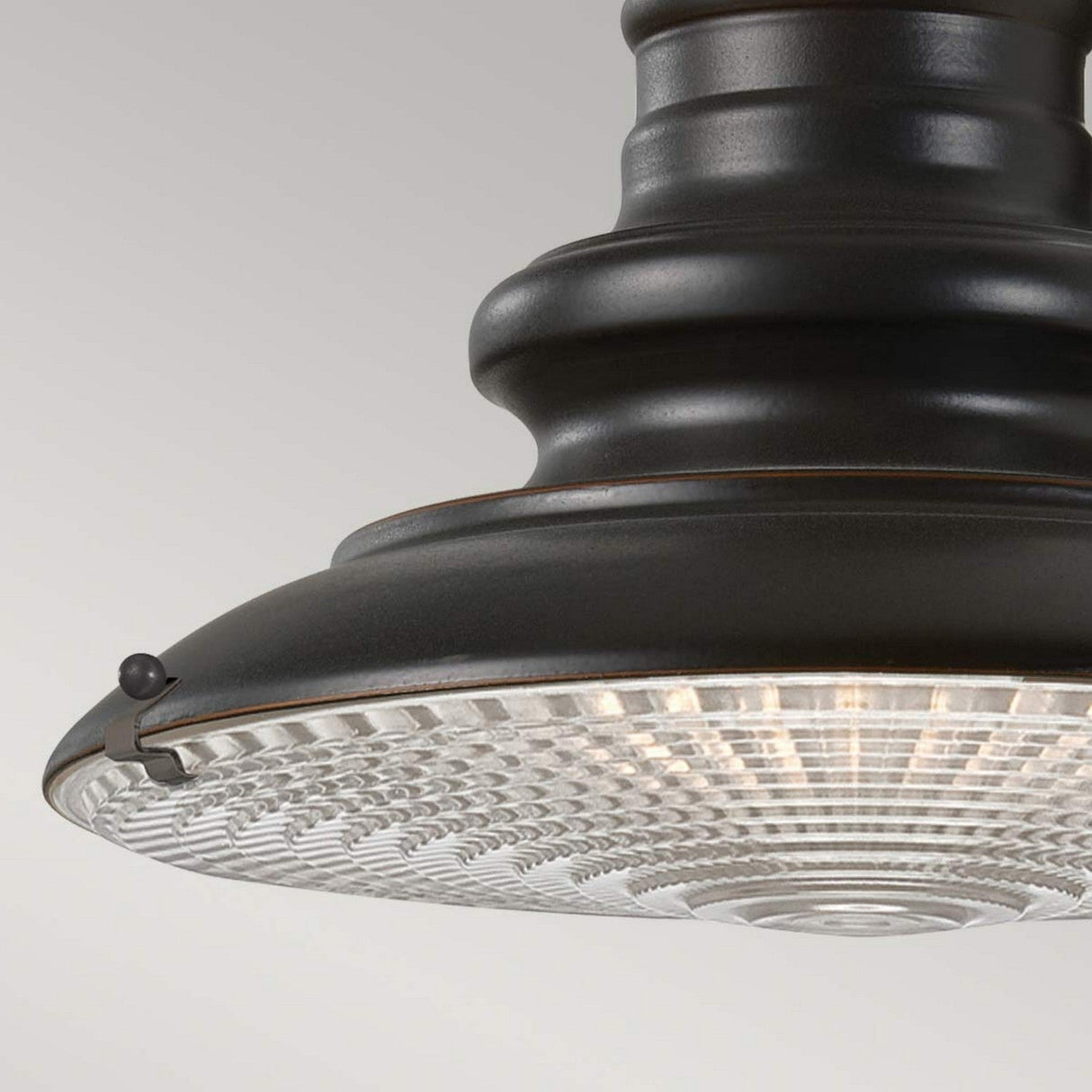 A detailed view of the Redding Station 1 Light Outdoor Small Wall Lantern in dark bronze, featuring a prismatic glass shade that masterfully diffuses light. The lantern showcases a vintage, industrial design with a robust metal frame and visible bolts.