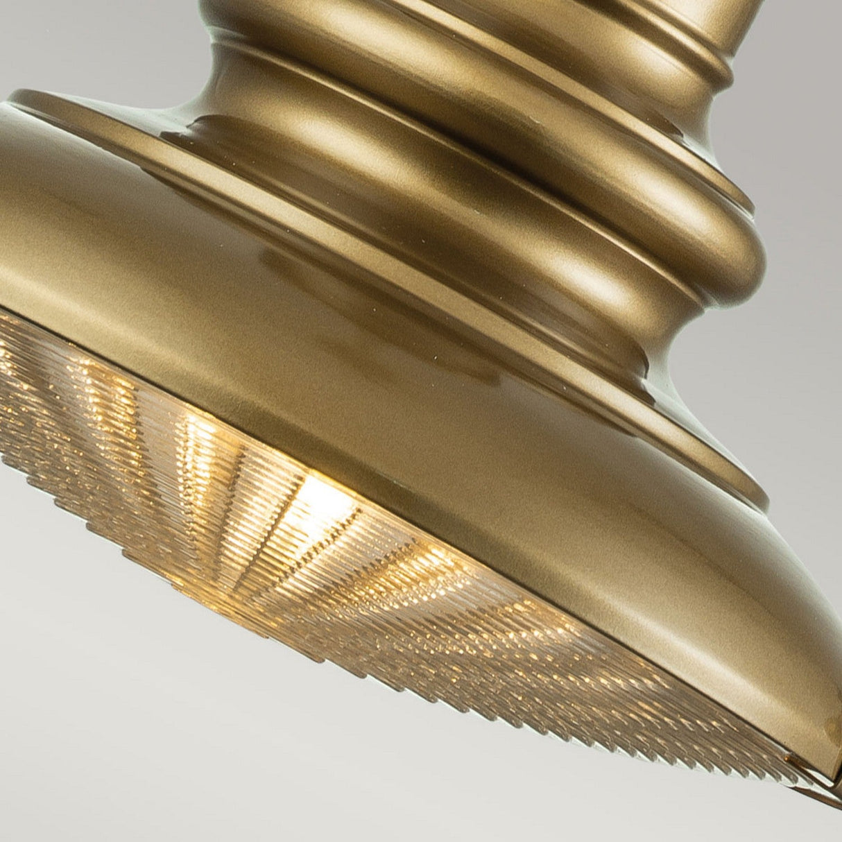 Close-up of the Redding Station 1 Light Outdoor Medium Chain Lantern in bronze, showcasing its gold-colored metal construction and textured, translucent shade that resembles prismatic glass. When lit, it casts a warm glow. The design includes smooth, rounded contours and vertical ridges on the stem, capturing the timeless charm of a vintage station lamp.