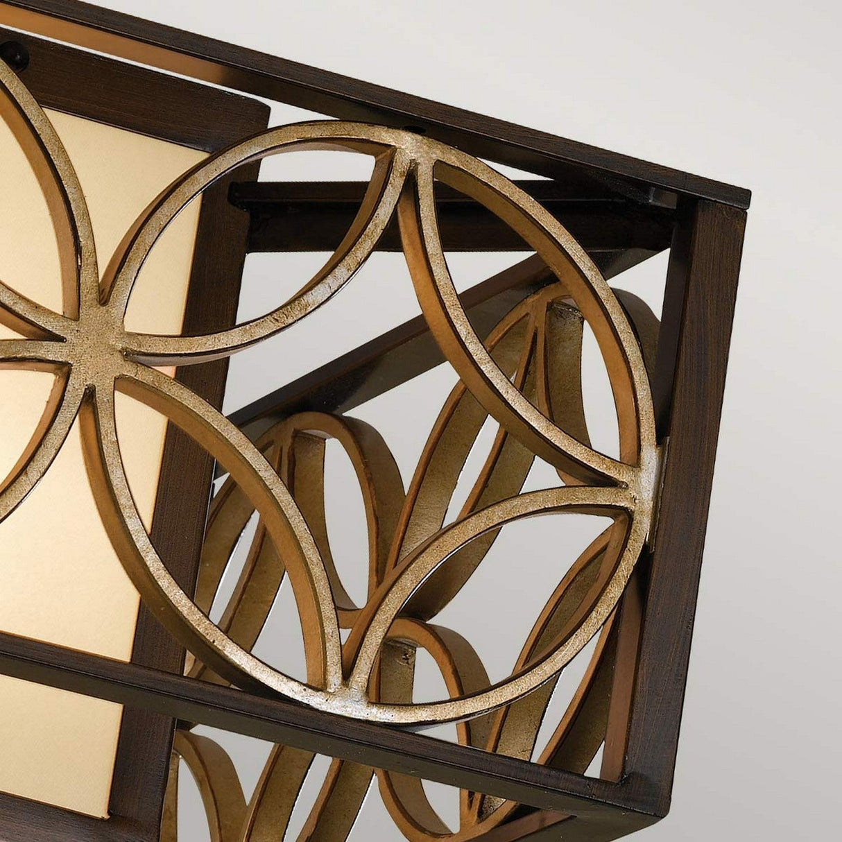 A detailed close-up of the Remy 2 Light Flush fixture highlights its complex geometric wooden patterns featuring intersecting circular shapes, which evoke the essence of French Arts and Crafts design. The harmonious blend of light and dark wood tones is beautifully enhanced by its Heritage Bronze and Parissiene Gold finish, all set against a neutral background.