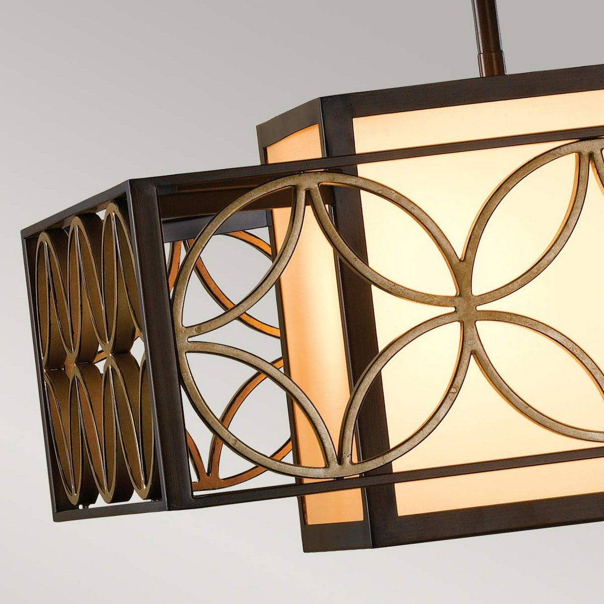 The Remy 1 Light Chandelier in Heritage Bronze and Parissiene Gold boasts a modern geometric design with interlocking circular patterns. Its dark metal frame highlights artisan craftsmanship while casting a soft, warm glow against the plain, light-colored background.