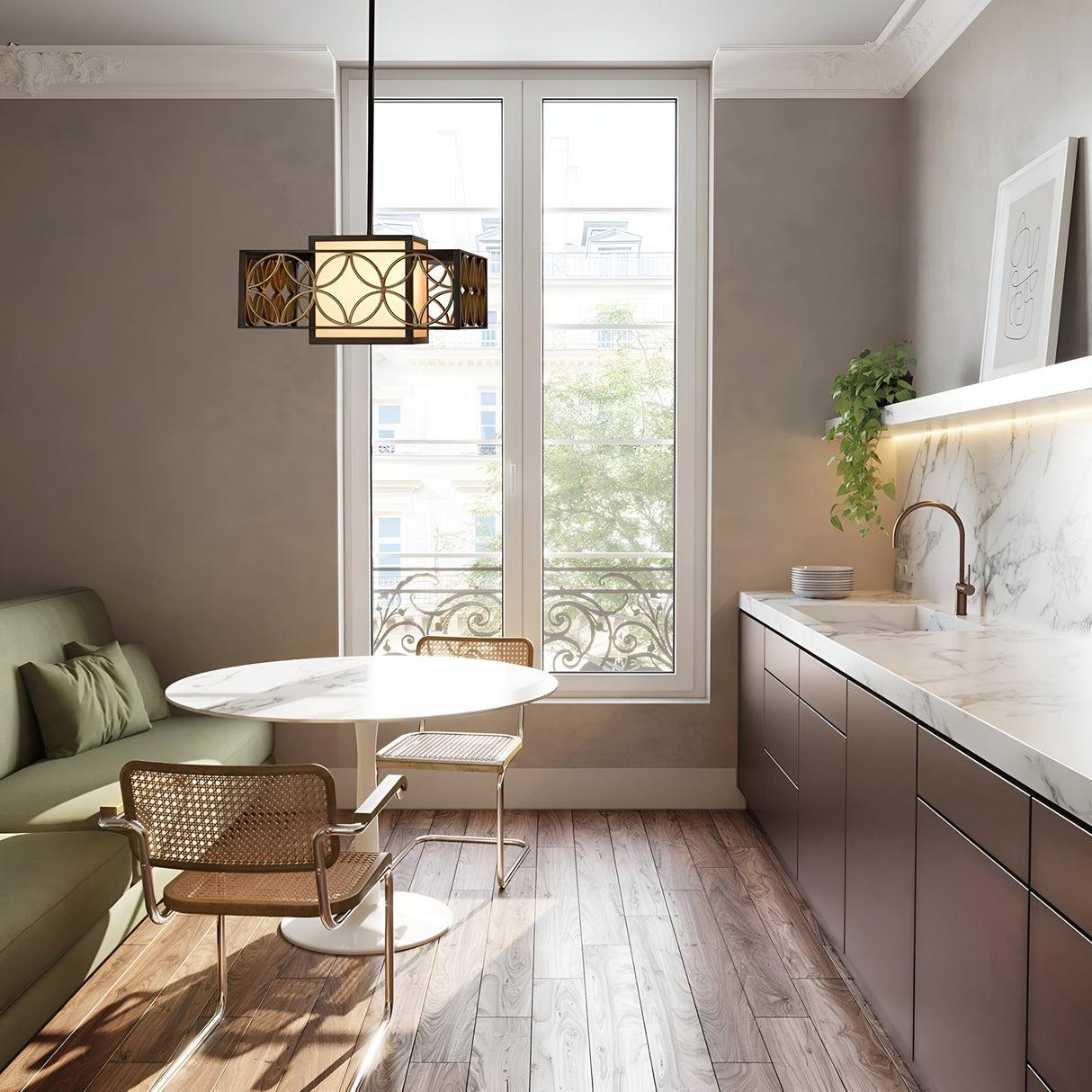 A contemporary kitchen is highlighted by a round marble table, two woven chairs, and a green sofa. The Remy 1 Light Chandelier in Heritage Bronze/Parissiene Gold elegantly hangs above, casting light on the marble countertop adorned with plants. A large window provides views of trees, and the wooden floor showcases artisan craftsmanship.