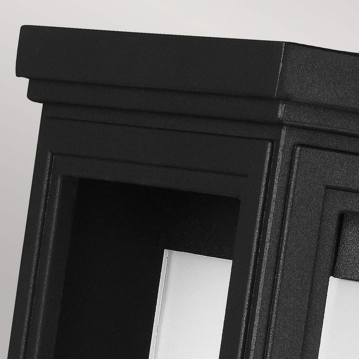 Close-up of the Roscoe 1 Light Outdoor Medium Wall Lantern in matte black, showcasing its sleek rectangular design with modern, sharp edges and geometric patterns. This weather-resistant wall lantern contrasts beautifully against the light gray background.